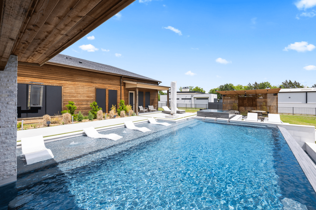 Geometric pool with sun loungers partly under wooden canopy.